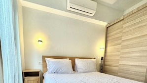 A neatly made bed with a white comforter and pillows, a wooden headboard, a bedside table with a lamp, and an air conditioning unit on the ceiling. - New apartment in the heart of Istanbul – near Istiklal and Galata (İstanbul)