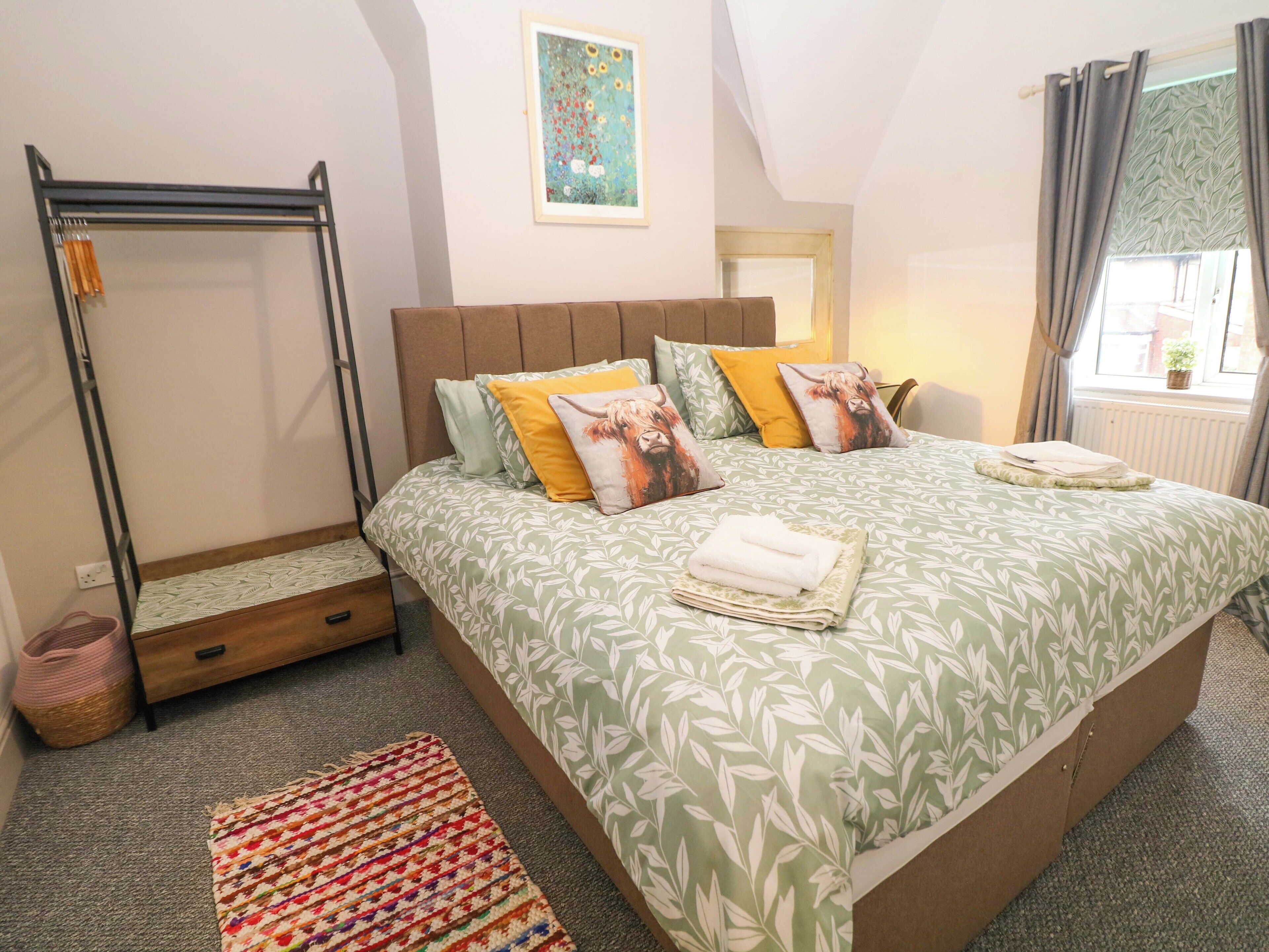 A bedroom with a bed, a hanging chair, a colorful rug, and a painting on the wall.