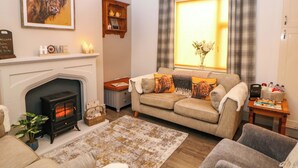 A cozy living room with a fireplace, a sofa set, and a large window with curtains. - Nightingale Cottage (Stafford)