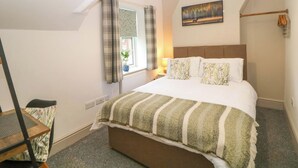 A bedroom with a bed, a window with curtains, a painting on the wall, and a lamp on the nightstand. - Nightingale Cottage (Stafford)