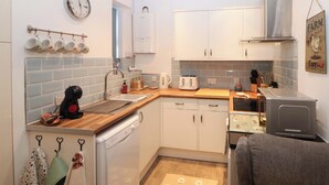 A compact kitchen with white cabinets, a dishwasher, a toaster, and a coffee maker. - Nightingale Cottage (Stafford)