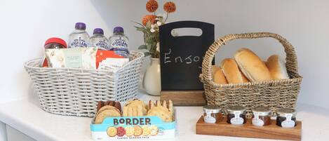A kitchen counter with a basket of bread, a box of biscuits, a jar of jam, and a bottle of milk.
