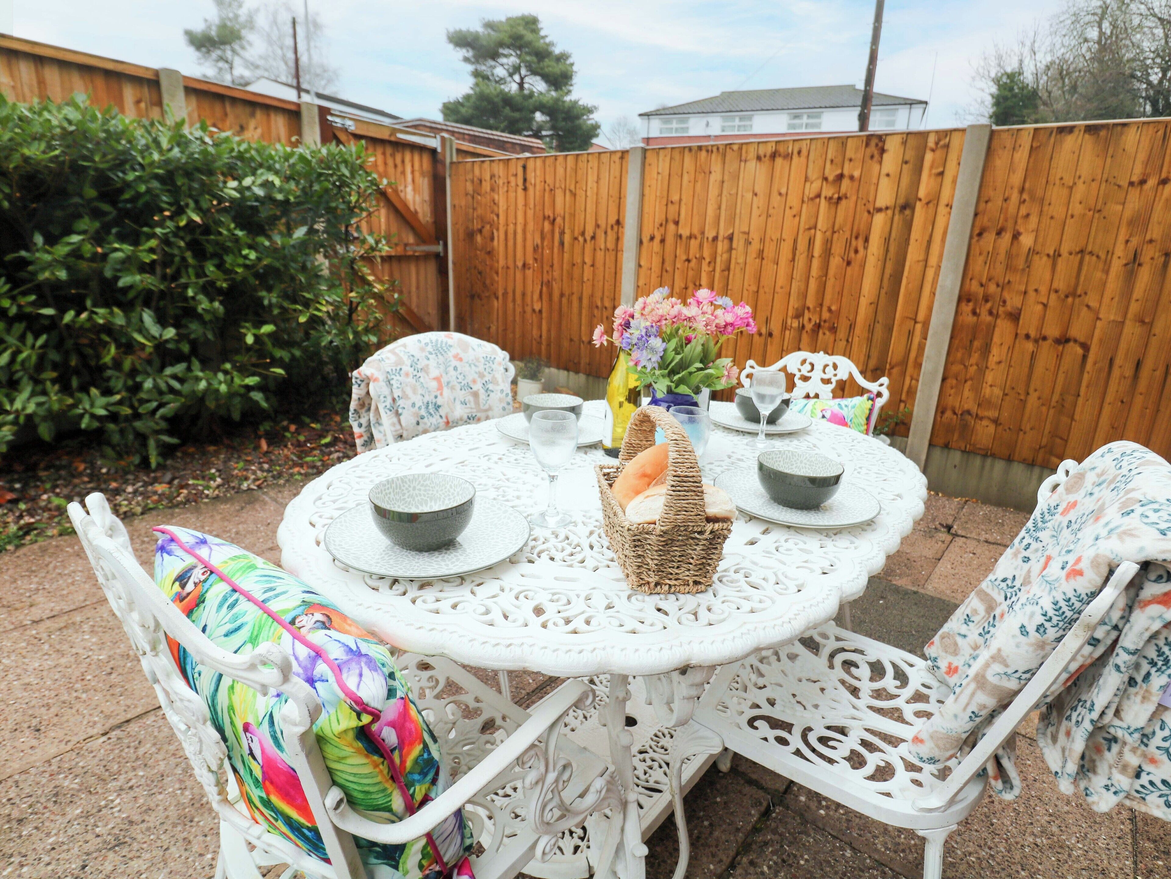 A round white table with four chairs, each with a colorful cushion. There are two bowls and two wine glasses on the table.