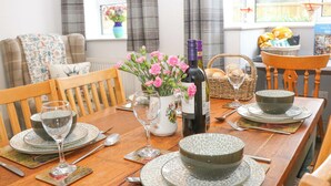 A dining table set with plates, glasses, and a bottle of wine, surrounded by chairs. - Nightingale Cottage (Stafford)