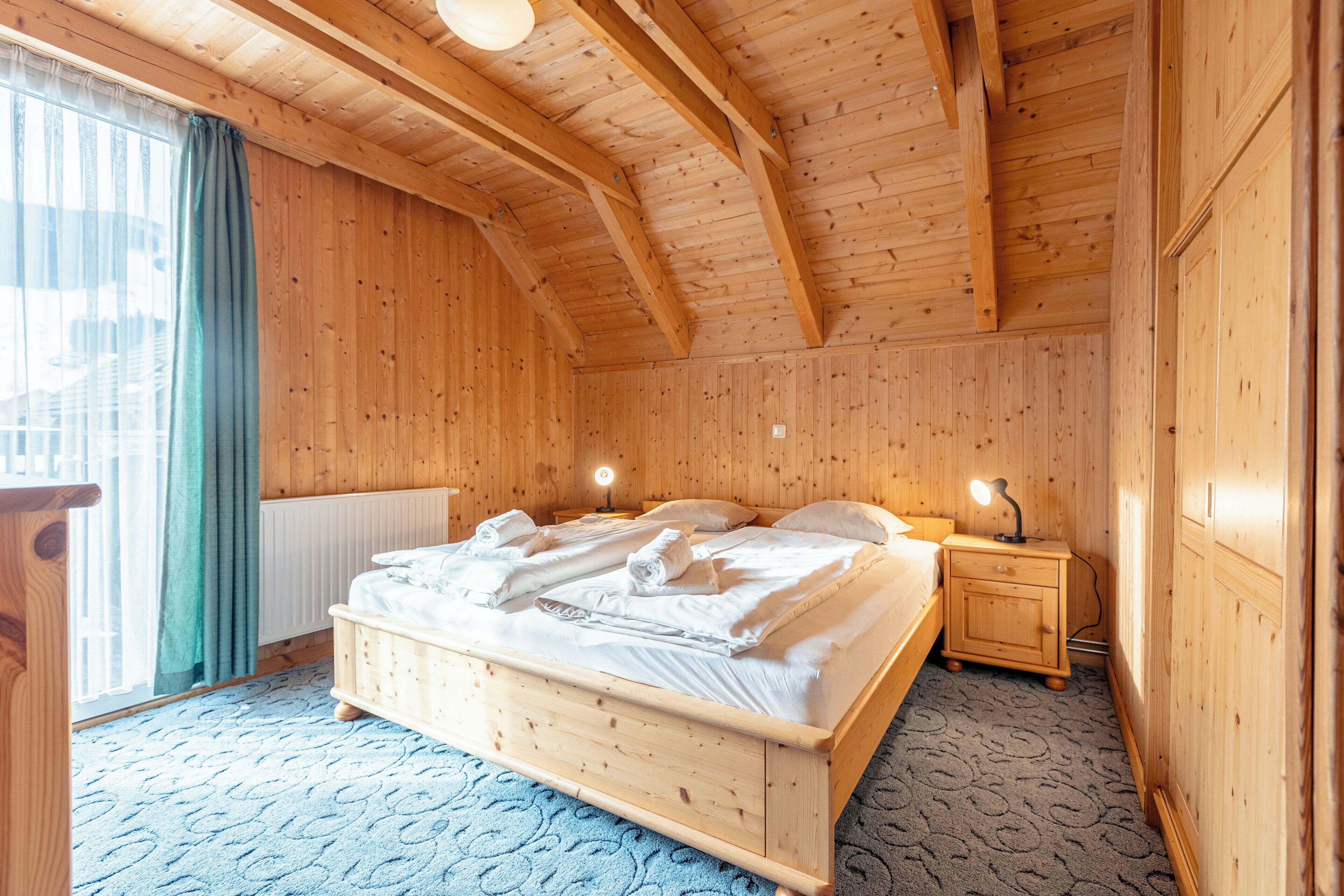 A wooden-paneled room with a bed, bedside tables, and a radiator.