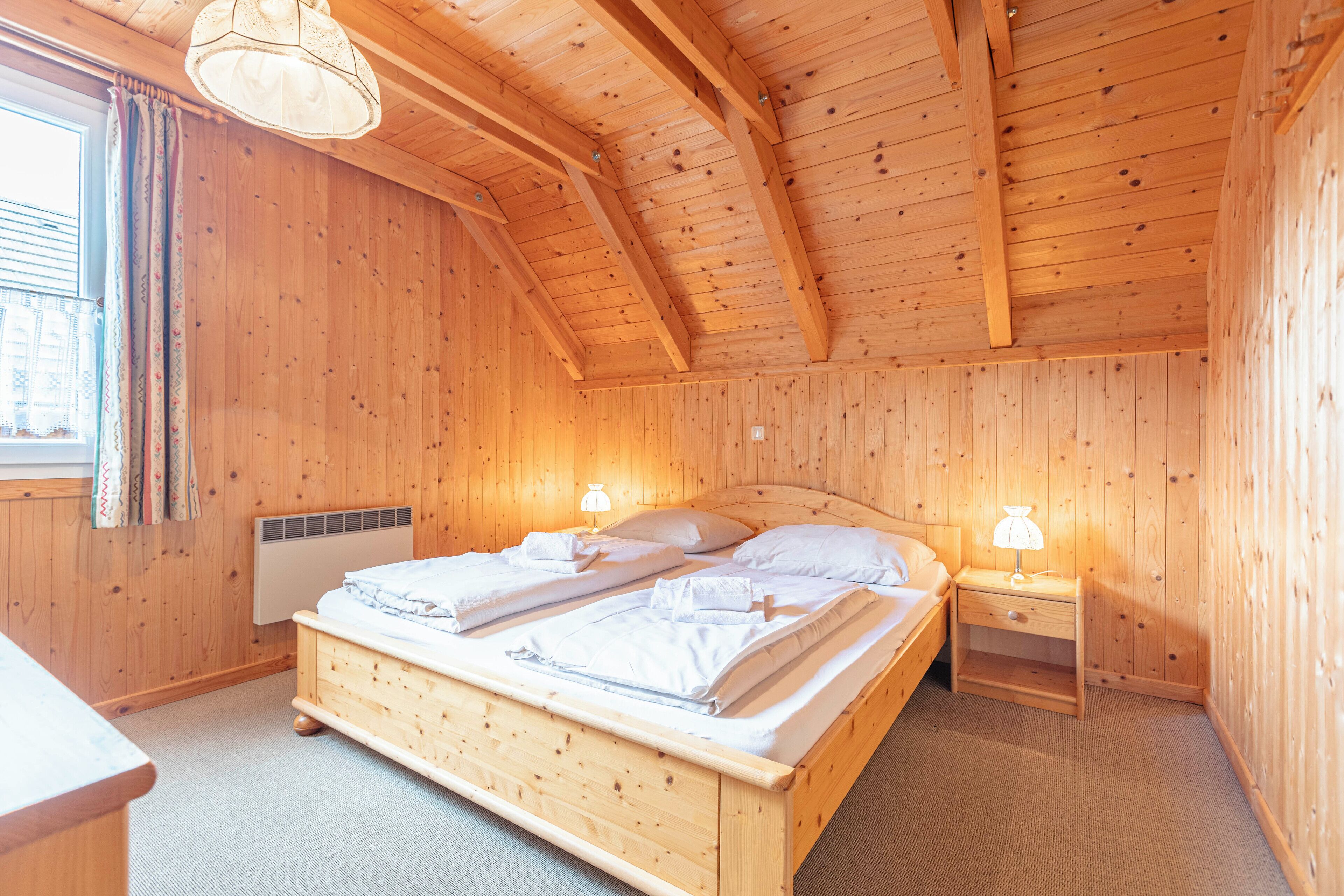 A wooden room with a bed, two bedside tables, and a window with curtains.