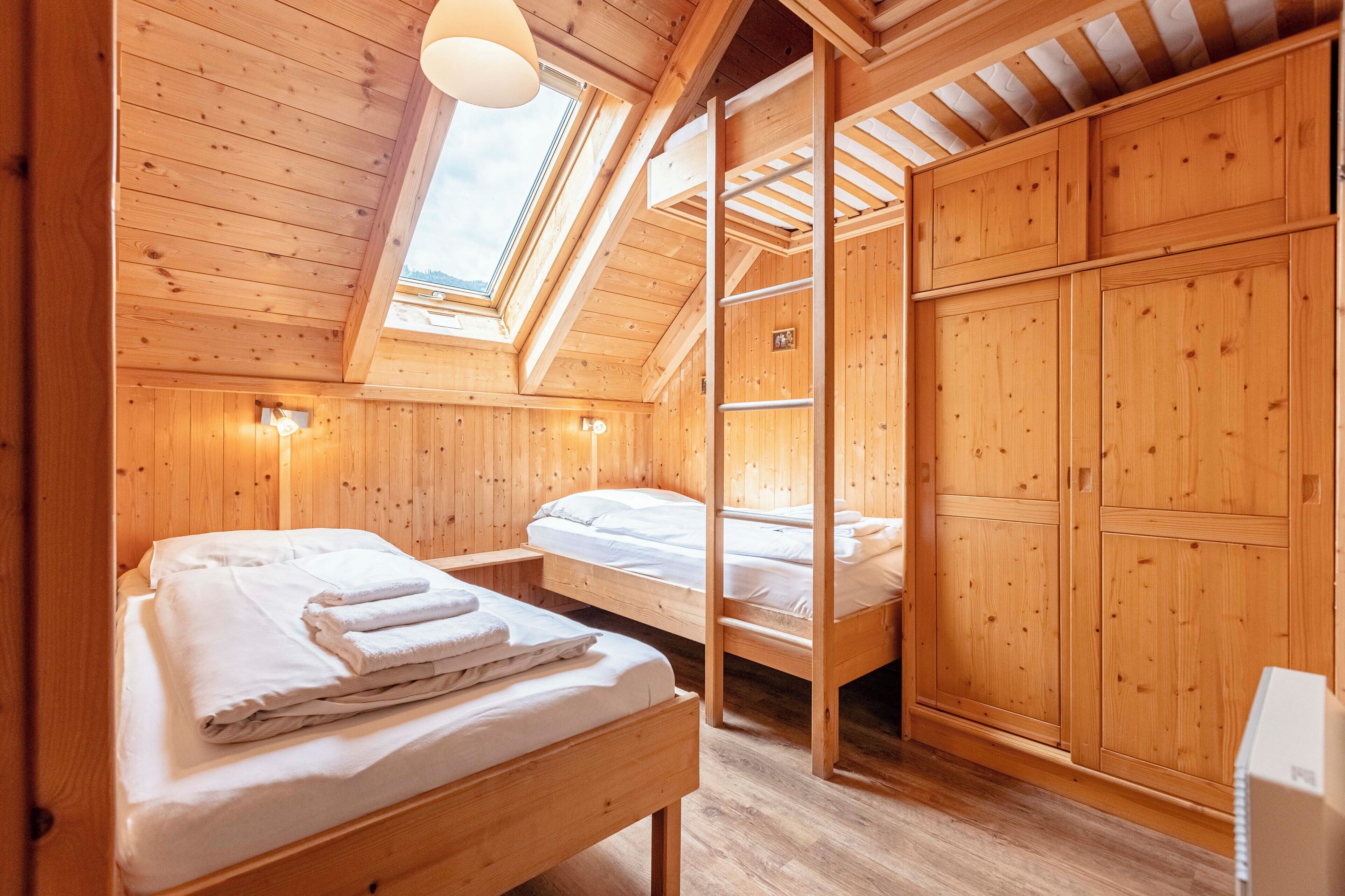 A wooden cabin with two bunk beds, a skylight, and a ladder leading to a loft area.