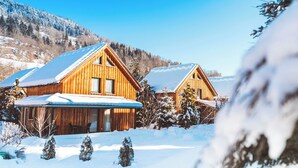 Two wooden cabins with snow-covered roofs, surrounded by a snowy landscape and trees. - FerienPark Kreischberg Ferienhäuser by ALPS RESORT (Sankt Lorenzen ob Murau)