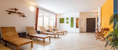 Una habitación amplia con sillones de madera y suelo de baldosas, un ventanal con cortinas y una puerta con letrero de salida de emergencia.