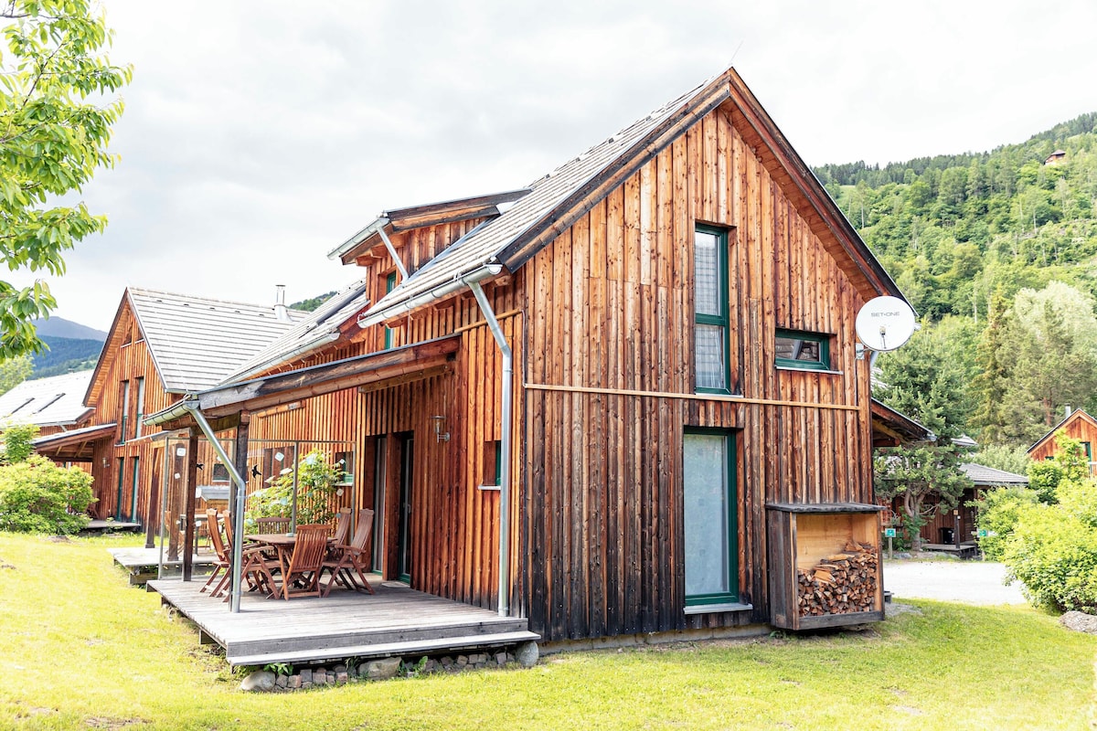 A wooden cabin with a porch, a satellite dish, and a stack of firewood.
