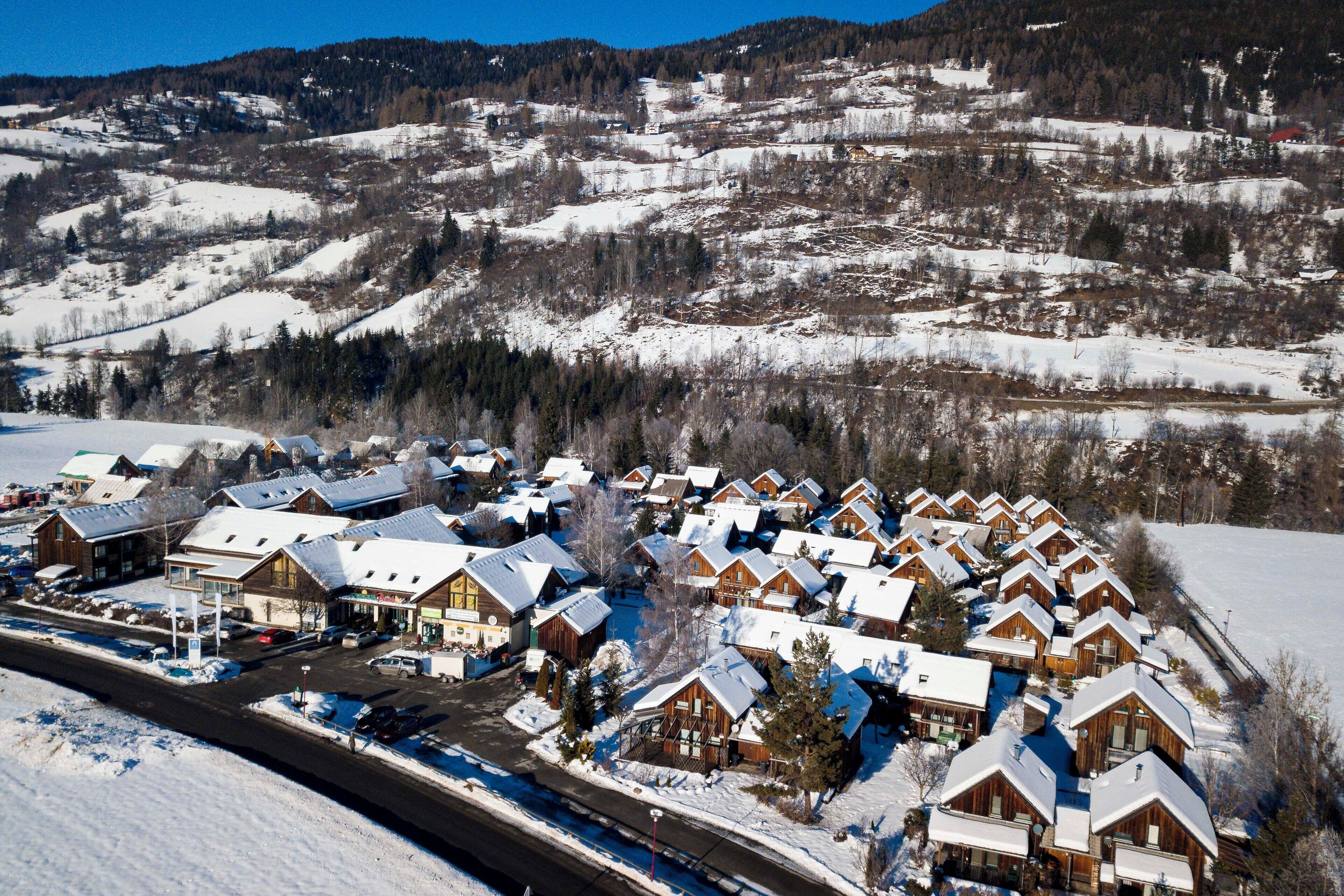 Ein verschneites Dorf mit Holzhäusern, einer Hauptstraße und einem Berg im Hintergrund.