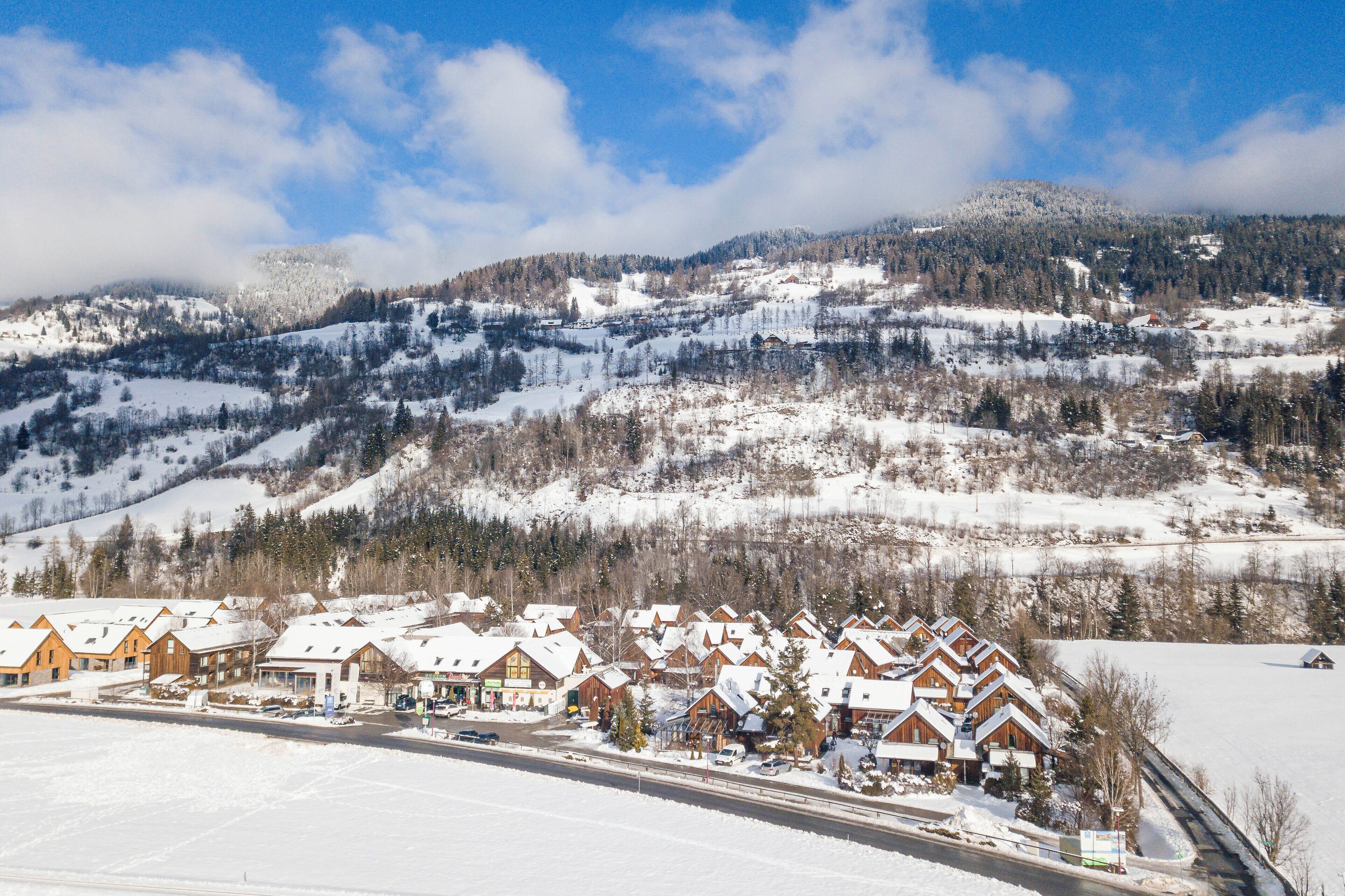 Vila coberta de neve com casas de madeira e montanhas ao fundo.