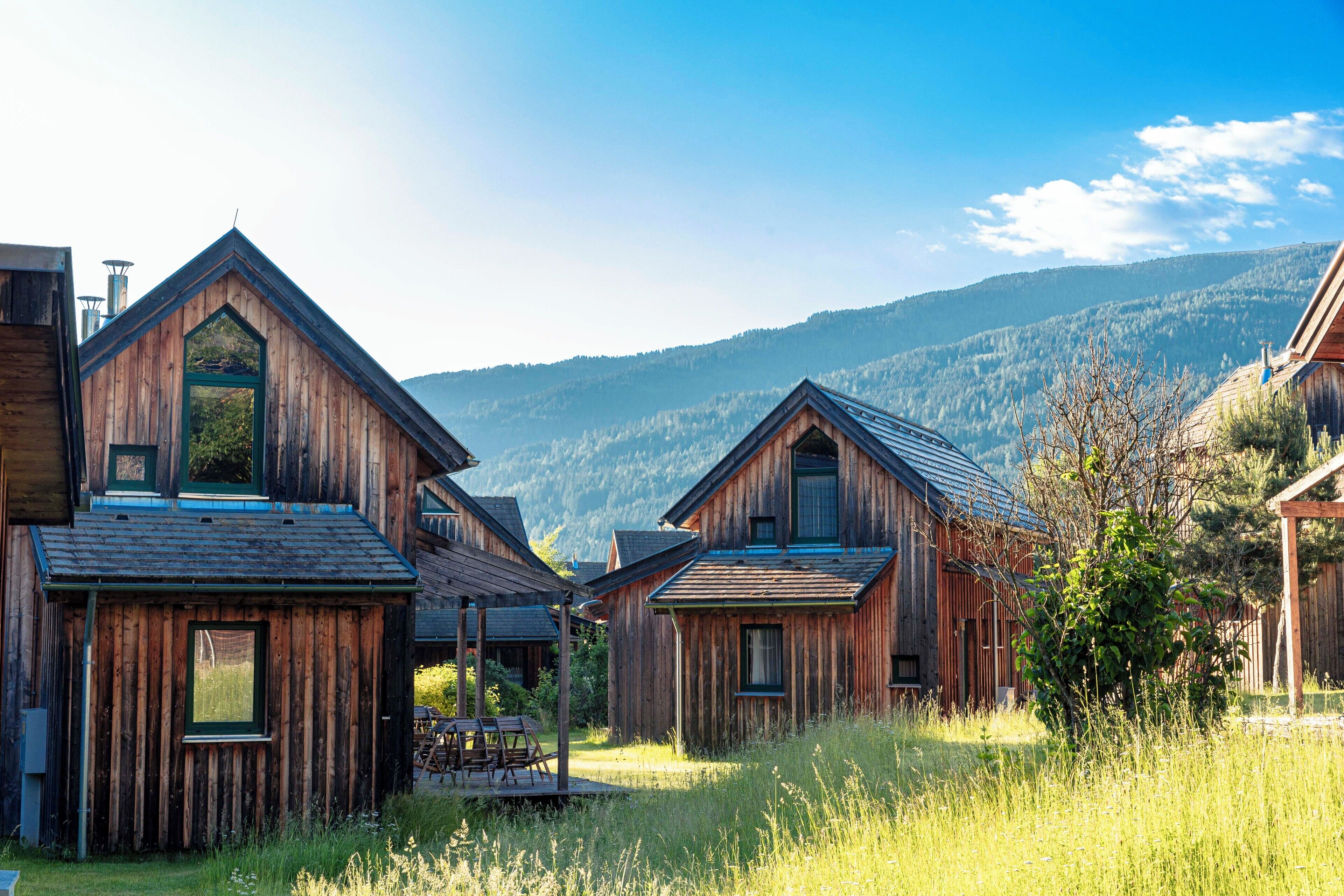 Una hilera de cabañas de madera con techos inclinados, rodeadas de pastos altos y montañas al fondo.