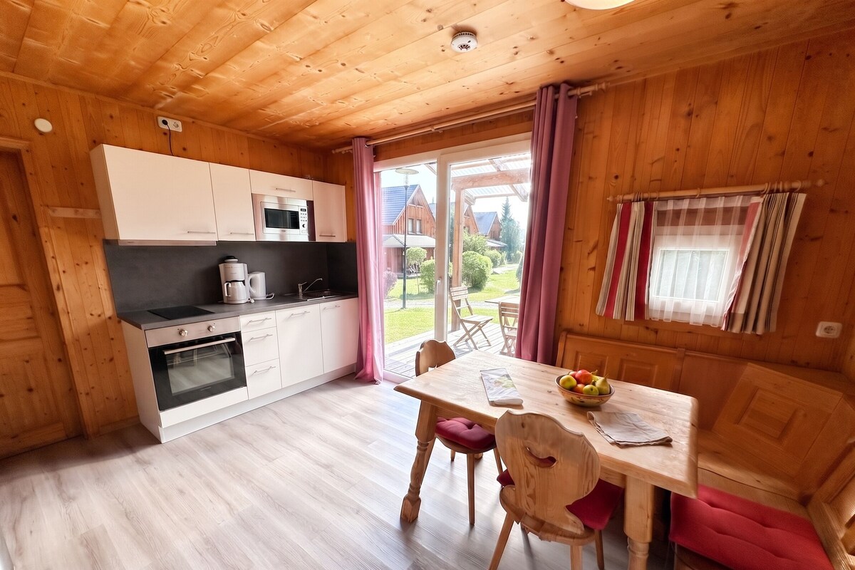 A compact kitchen with a microwave, oven, and coffee maker. There's a dining table with chairs and a bowl of fruit.