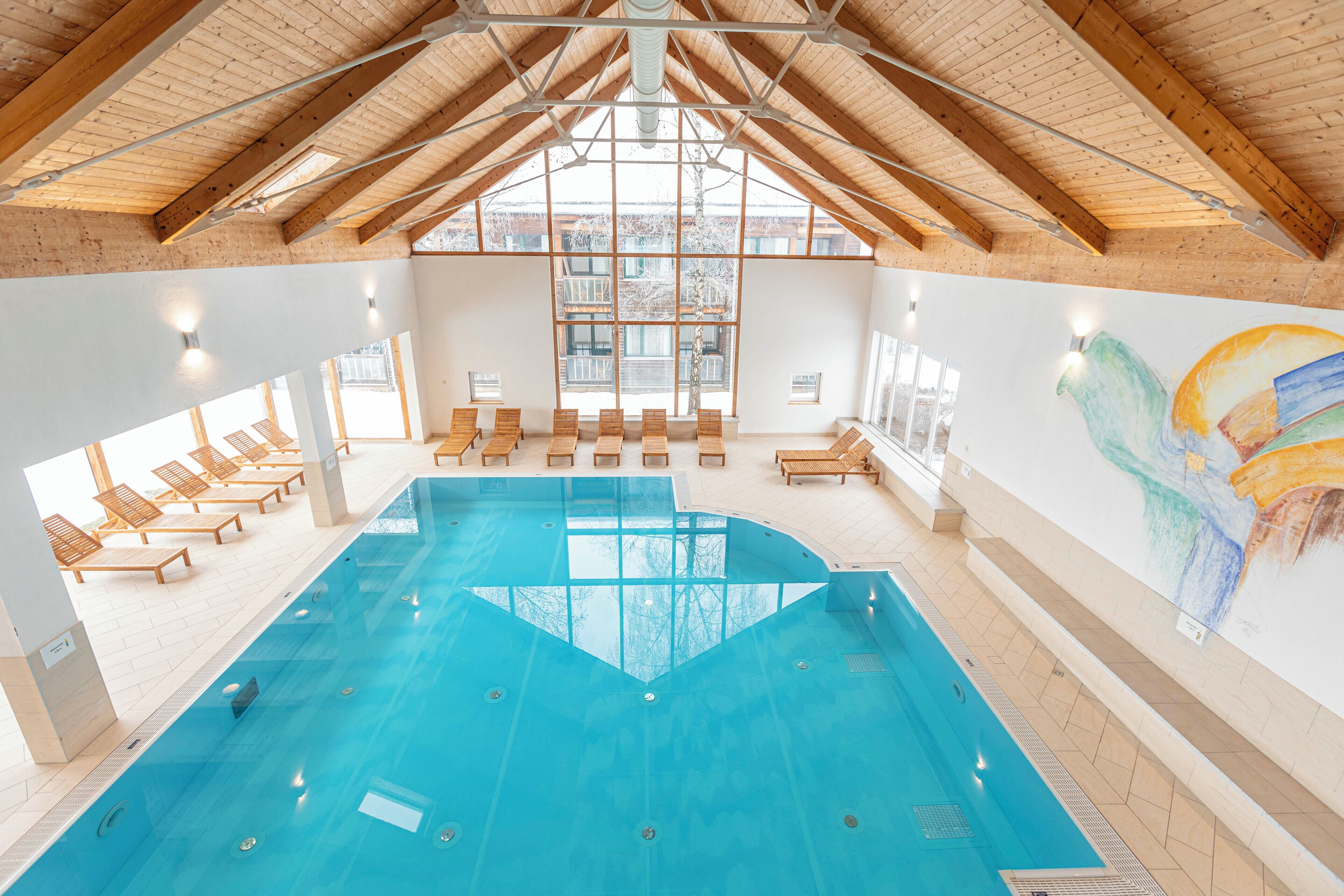 An indoor swimming pool with wooden beams, sunlit seating areas, and a large window.