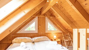 A cozy attic bedroom with a wooden ceiling, two windows, a bed with white linens, and a nightstand with a lamp. - FerienPark Kreischberg Ferienhäuser by ALPS RESORT (Sankt Lorenzen ob Murau)