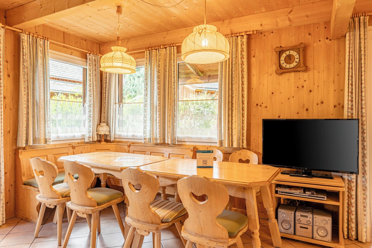 A wooden interior with a dining table, chairs, a TV, and a clock on the wall.