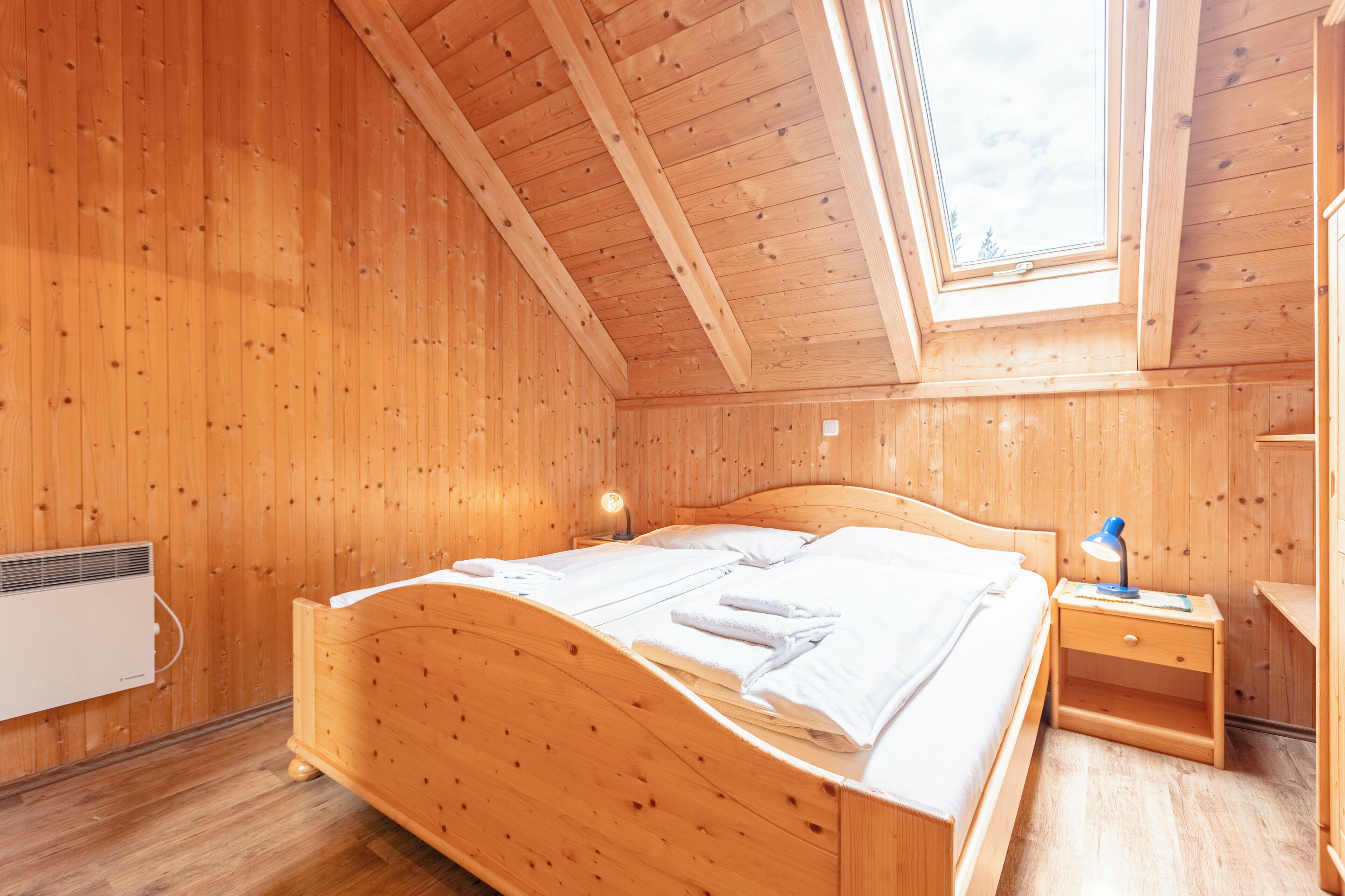 A wooden room with a bed, a nightstand, and a skylight.