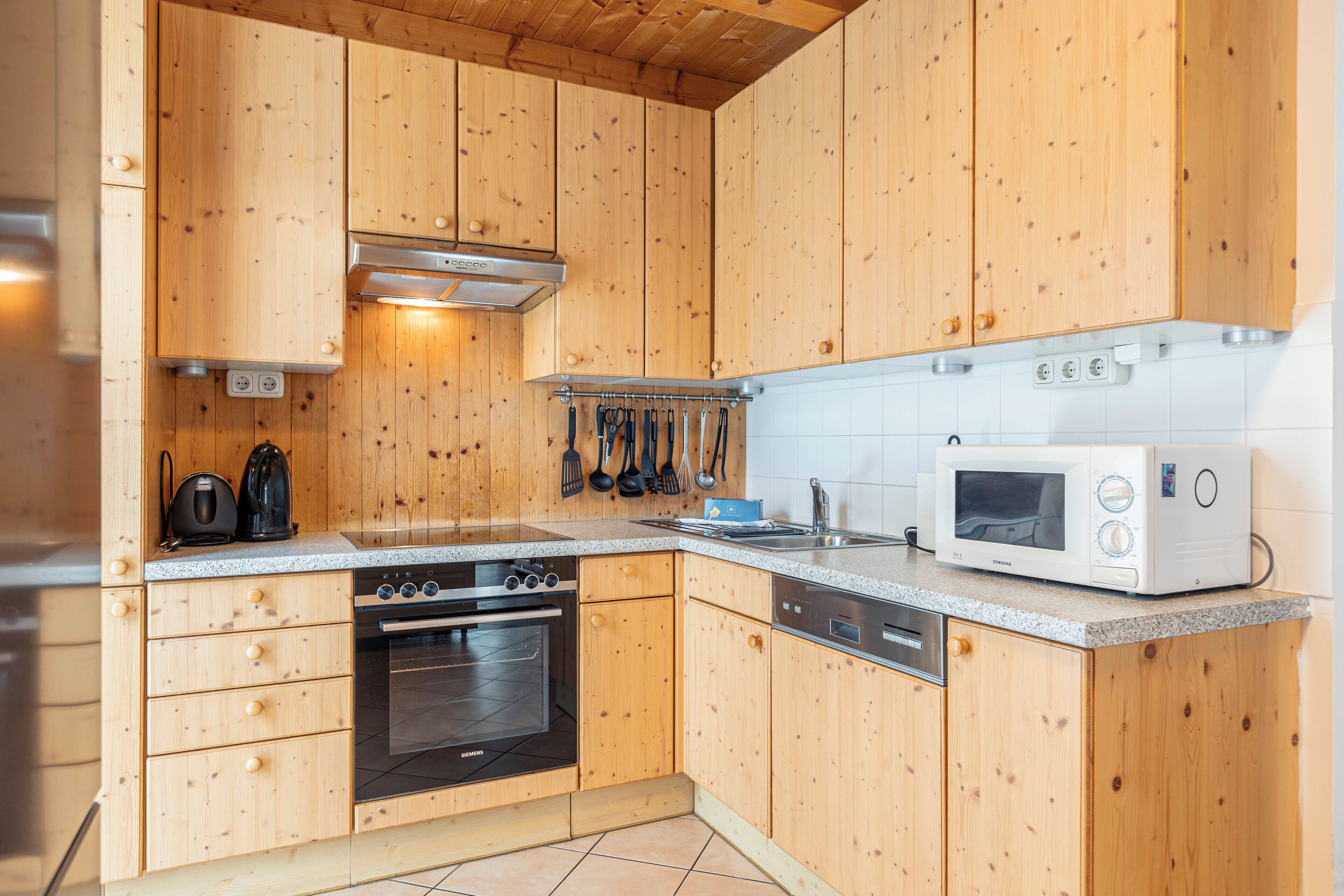 Cozinha compacta com armários de madeira, forno embutido, micro-ondas e exaustor de aço inoxidável.