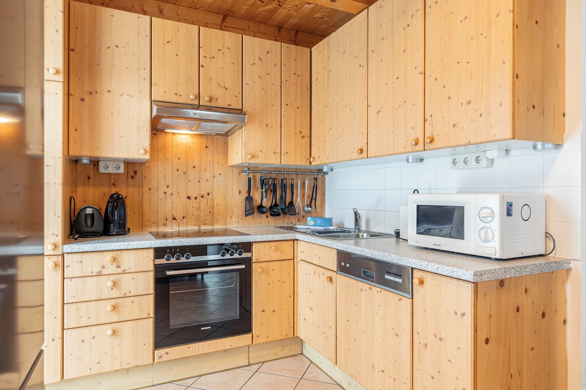 A compact kitchen with wooden cabinets, a built-in oven, a microwave, and a stainless steel range hood.