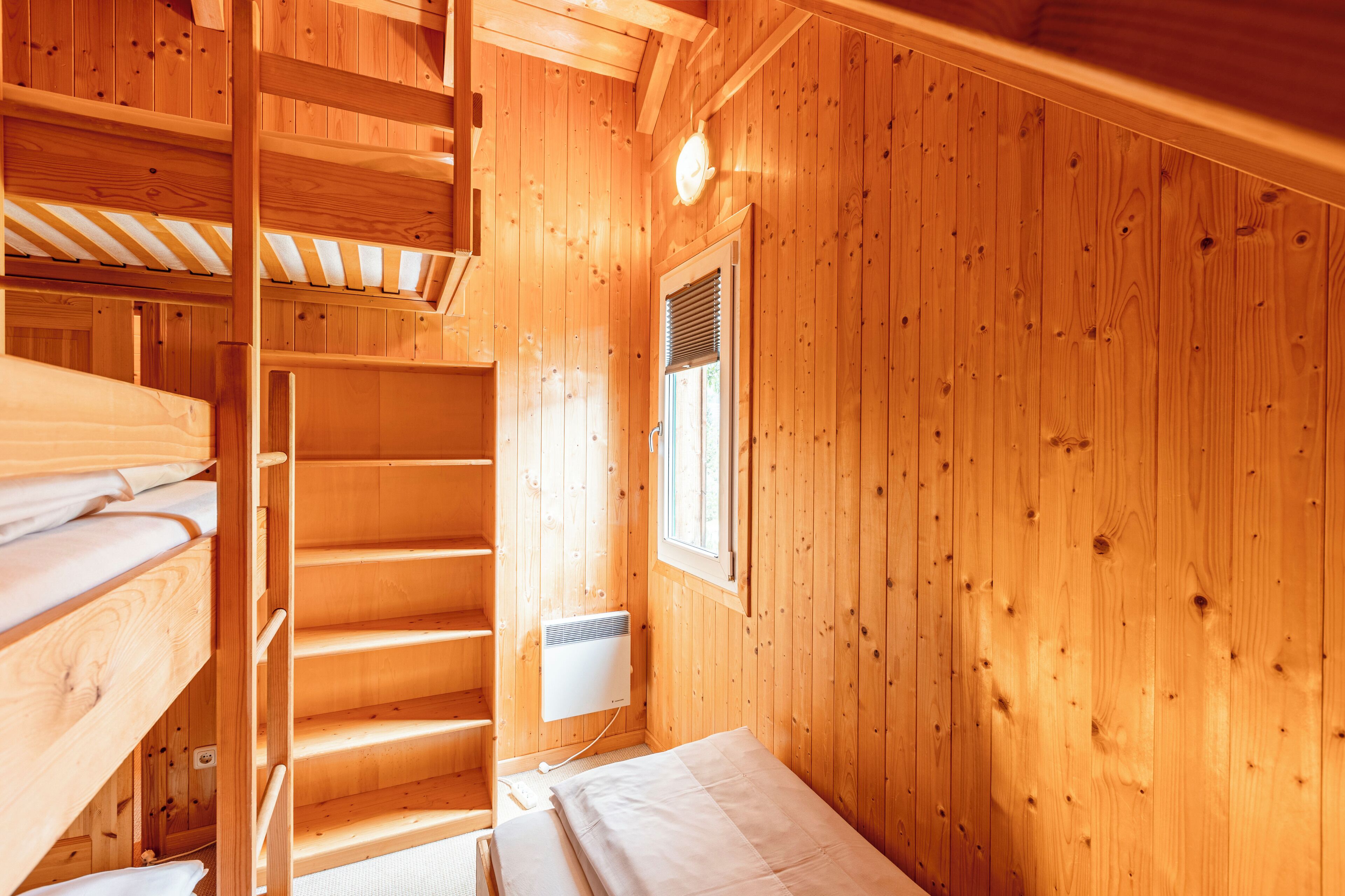 A wooden cabin with bunk beds, a window, and a wall-mounted heater.