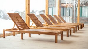 A row of wooden lounge chairs with a view of a snowy landscape through large windows. - FerienPark Kreischberg Ferienhäuser by ALPS RESORT (Sankt Lorenzen ob Murau)