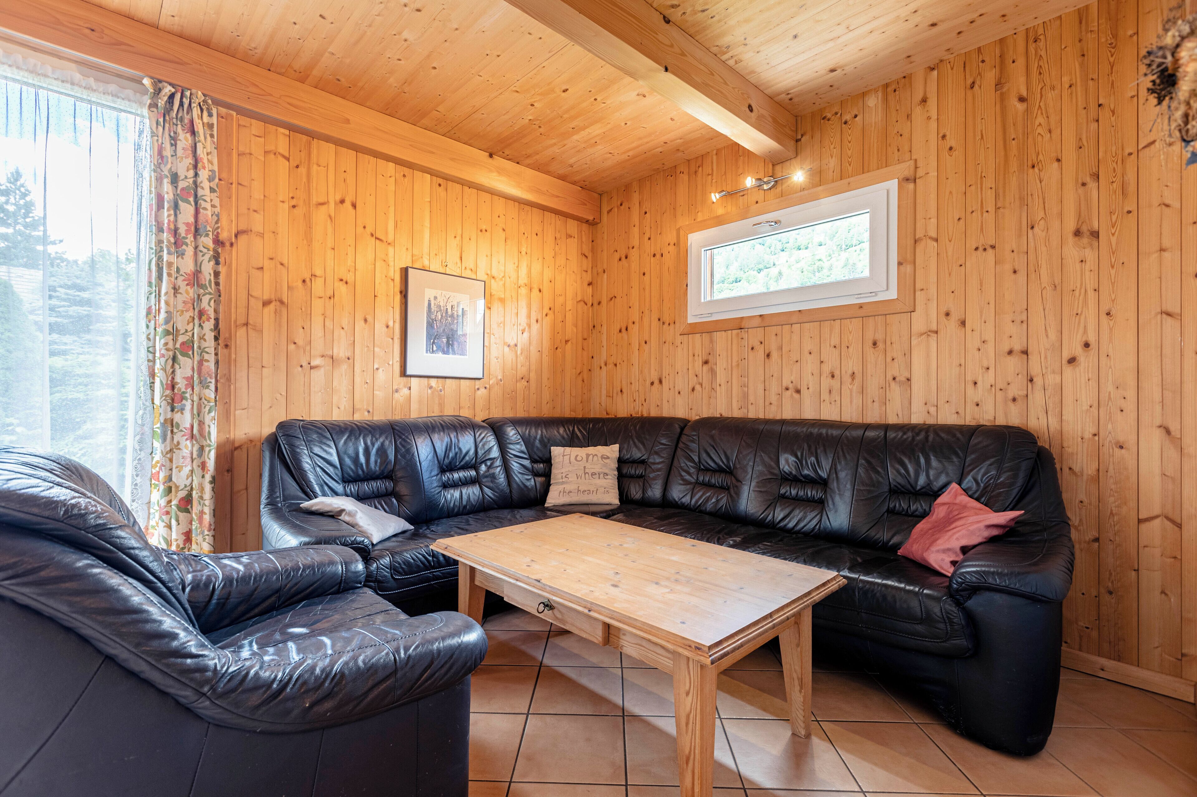 Une pièce chaleureuse avec des murs en bois, un canapé en cuir noir, une table basse en bois et une fenêtre avec des rideaux.