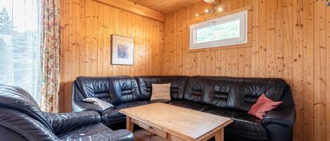 Une pièce chaleureuse avec des murs en bois, un canapé en cuir noir, une table basse en bois et une fenêtre avec des rideaux.