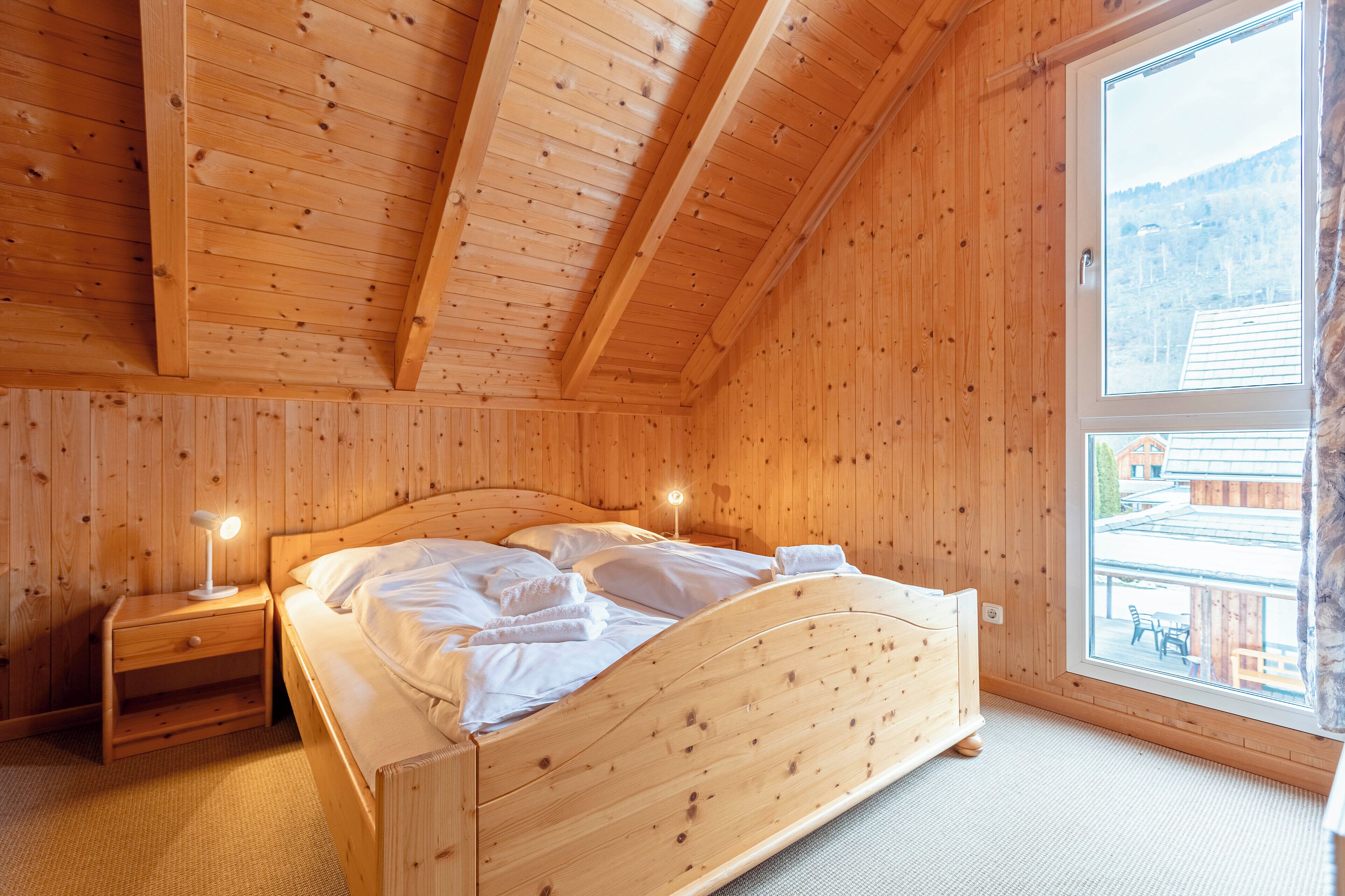 Een houten kamer met een bed, nachtkastje en raam.