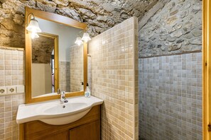 A bathroom with a stone wall, a wooden vanity, a sink, and a mirror with lights.