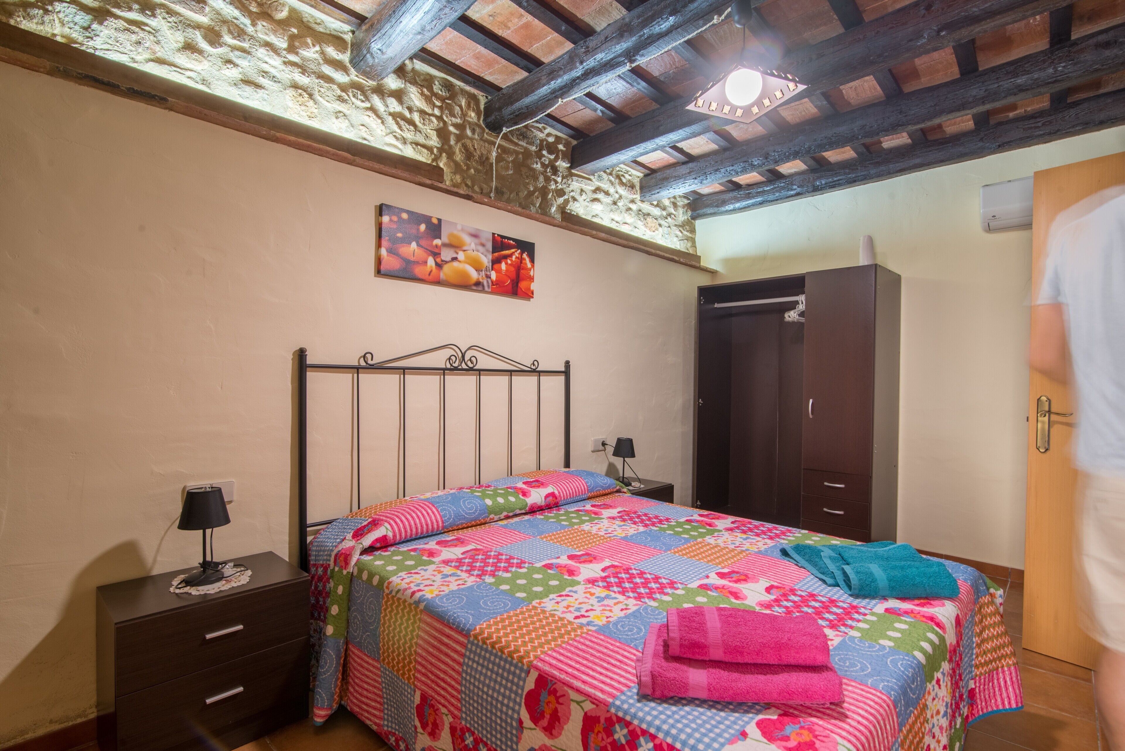 Een slaapkamer met een bed, nachtkastje, kledingkast en een plafond met zichtbare balken.