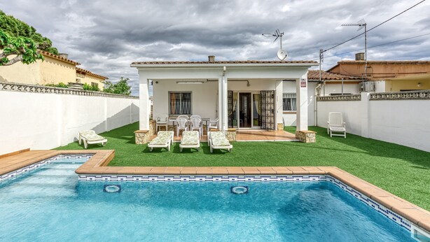 Ein Swimmingpool mit Liegestühlen, eine überdachte Terrasse und ein weißes Gebäude mit einem Ziegeldach.