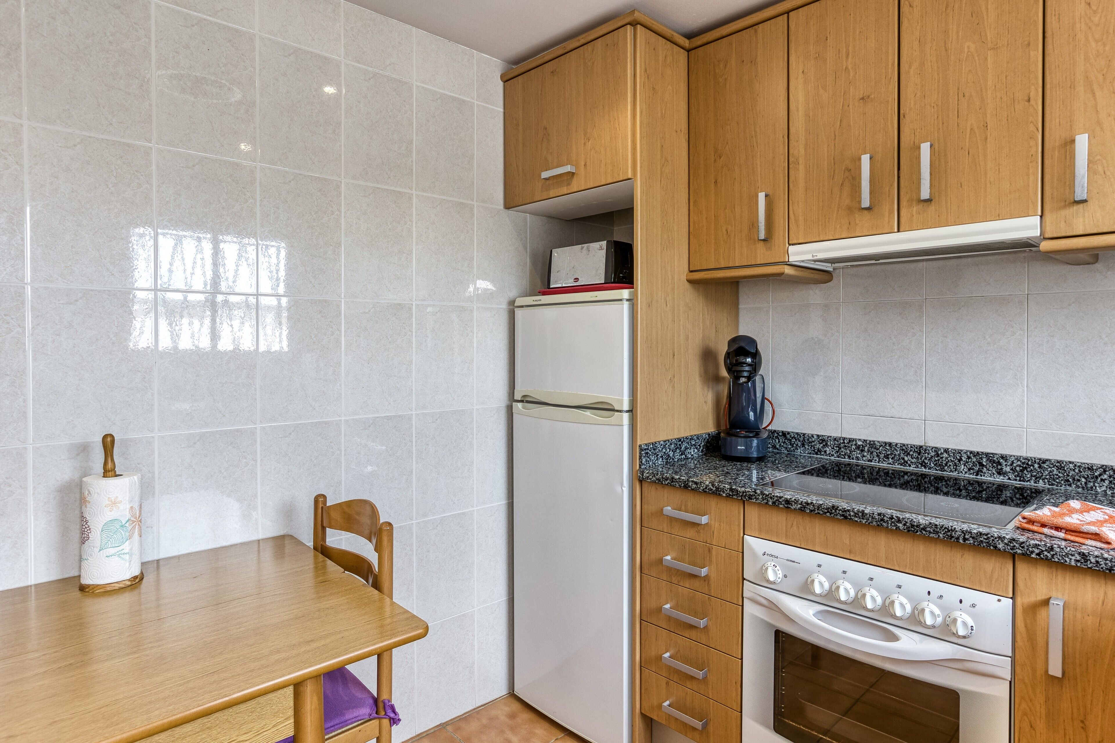 A compact kitchen with a refrigerator, stove, and wooden cabinets.