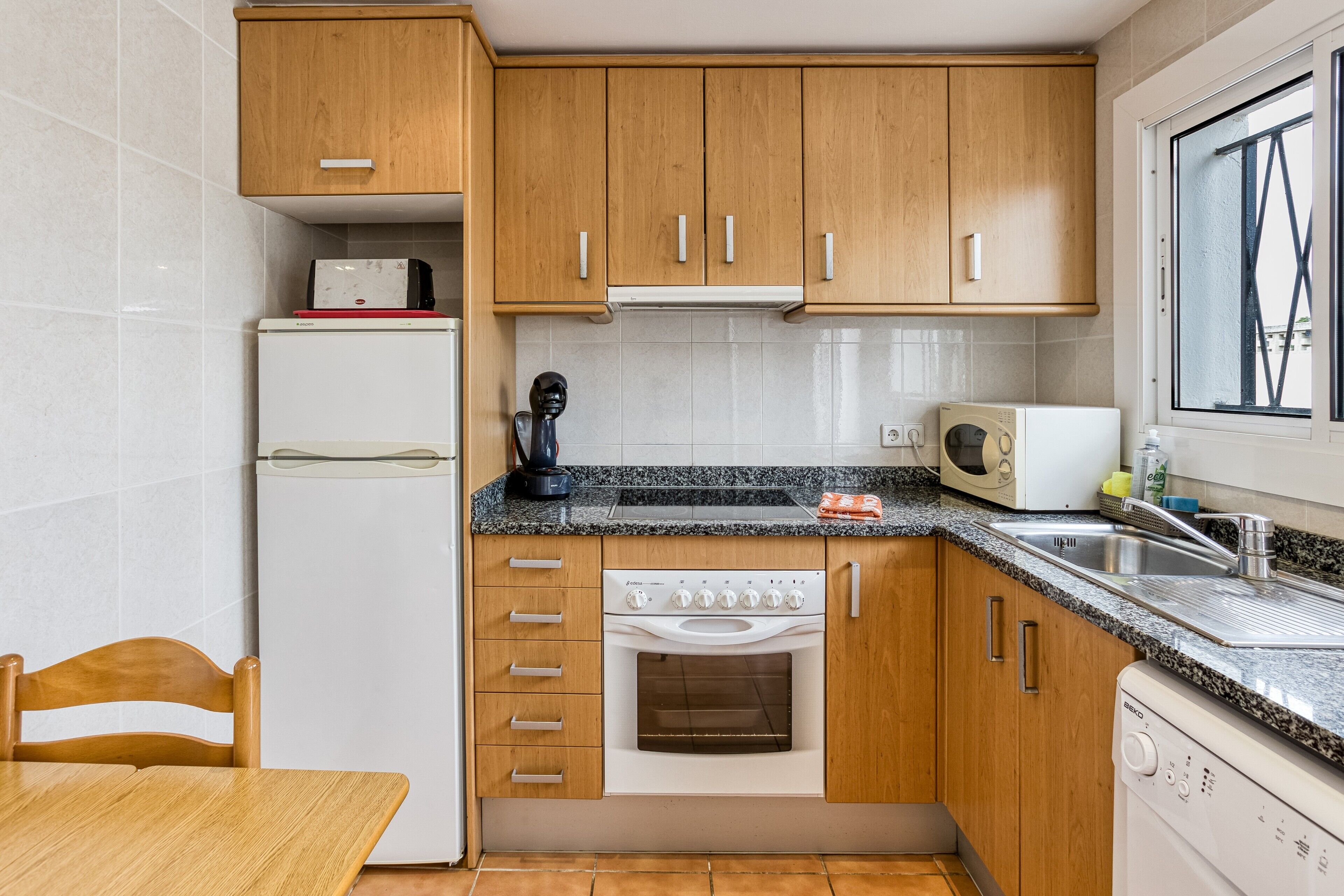 A compact kitchen with wooden cabinets, a built-in oven, a microwave, and a dishwasher.