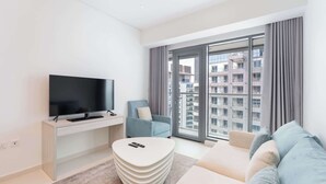 Ein modernes Wohnzimmer mit einem Flachbildfernseher, einem hellblauen Sessel, einem beigen Sofa und einem großen Fenster mit Blick auf die Stadt.