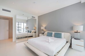 A modern hotel room with a large bed, bedside lamps, a mirror, and a view of the city. - StayShort - Prime 2 Bedroom Sleeps 4 in Palm Jumeirah (Palm Jumeirah)