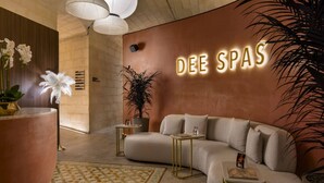 A modern interior with a curved sofa, a large potted plant, and a wall-mounted sign reading 'DEE SPAS'. - Mercury Towers Luxury Stay w/ Rooftop Pool & Views (St. Julian`s)