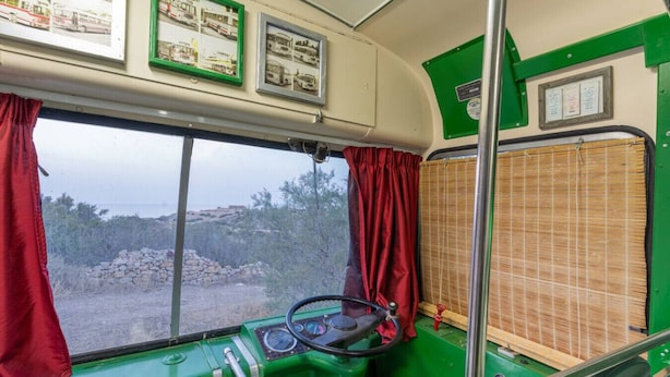 L'intérieur d'un autobus, avec un volant, un tableau de bord et une fenêtre ornée de rideaux rouges.
