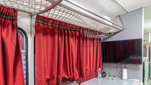 Un compartiment de train compact comprenant un canapé, des coussins rouges, une petite table et un téléviseur.
