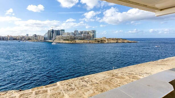 Paisagem costeira com edifícios modernos, uma praia arenosa e um mar azul e límpido.