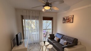 A living room with a sofa, a TV, a ceiling fan, and a dining area with a table and chairs. - Central Studio in Cannes Near The Martinez- 2351 (Cannes)