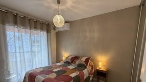 A bedroom with a large bed, a bedside table with a lamp, a clear chair, and a window with curtains. - Central Studio in Cannes Near The Martinez- 2351 (Cannes)