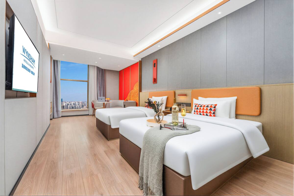 Ein Hotelzimmer mit Blick auf die Stadt, zwei Betten, einem Fernseher und einem kleinen Tisch mit einer Flasche und Gläsern.