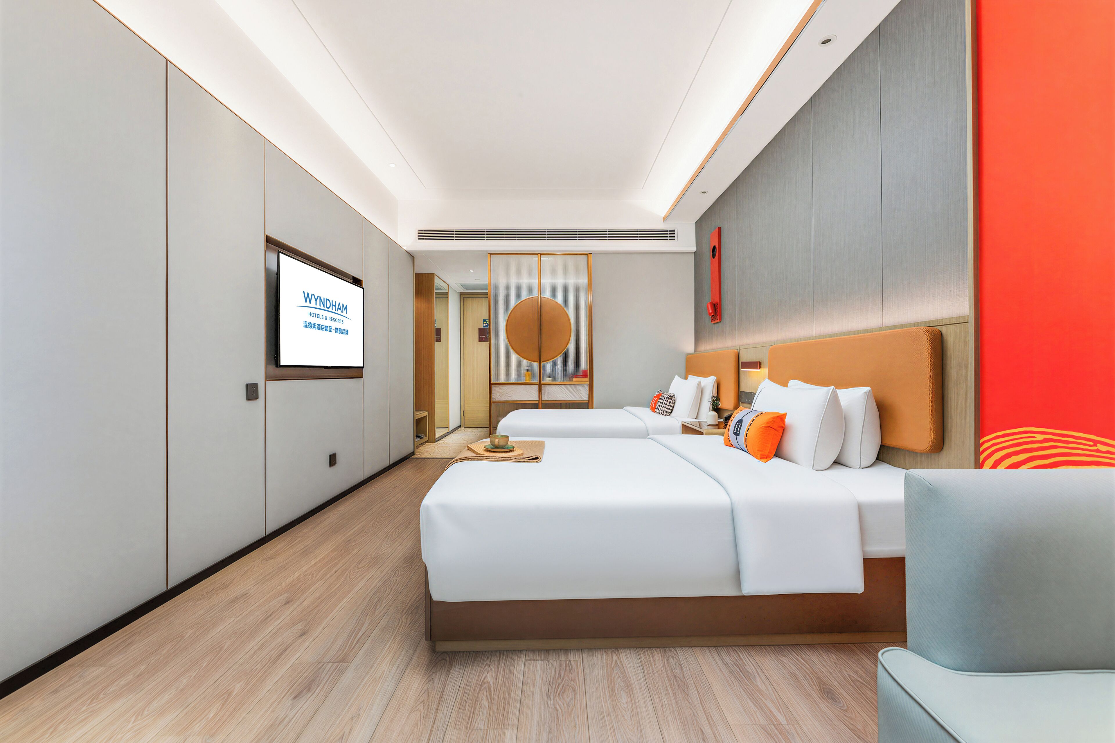 A modern hotel room with a large bed, a sofa, and a TV displaying 'Wyndham Hotels & Resorts'.