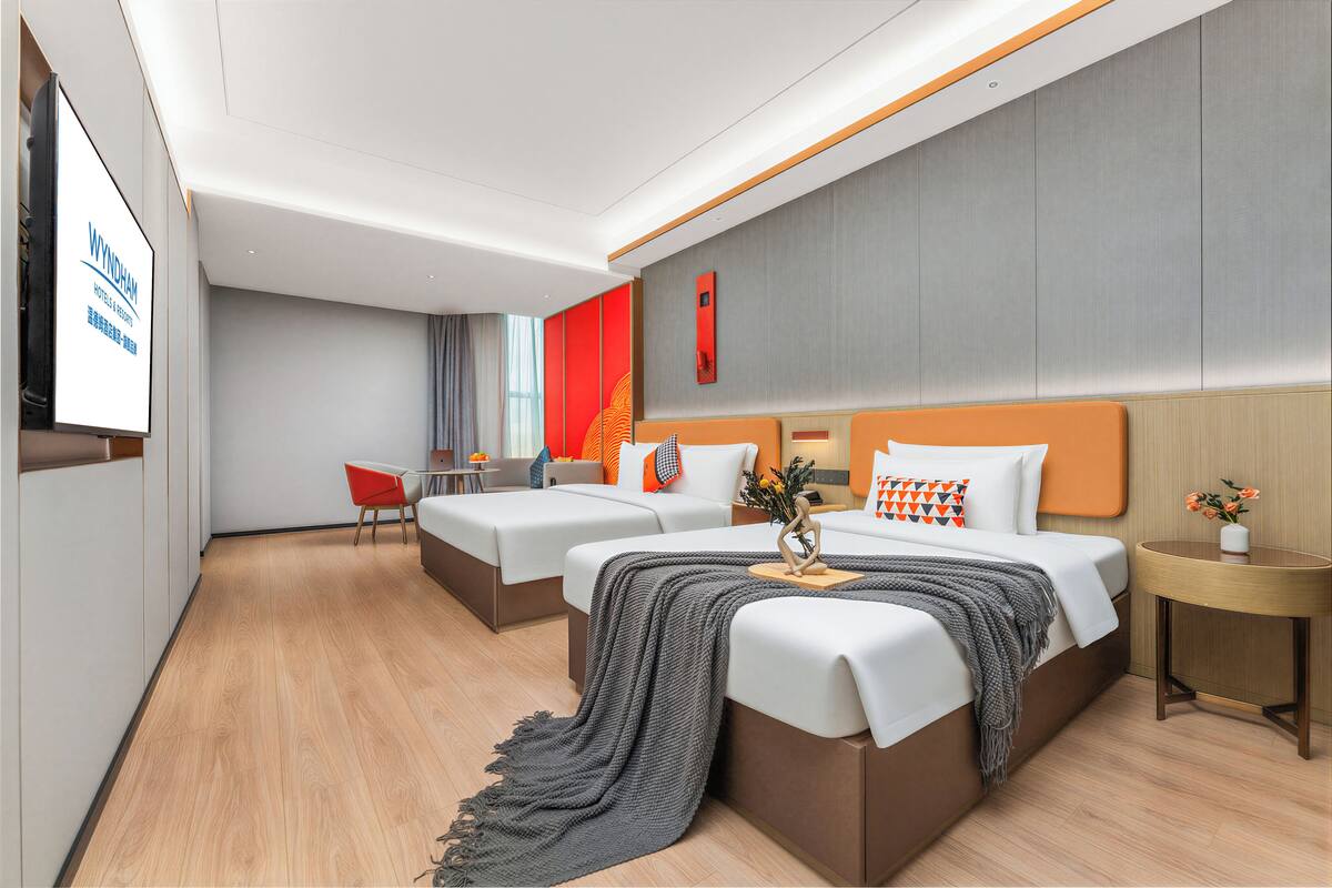 Ein Hotelzimmer mit zwei Betten, einem kleinen Tisch, einem Sessel und einem Fernseher.