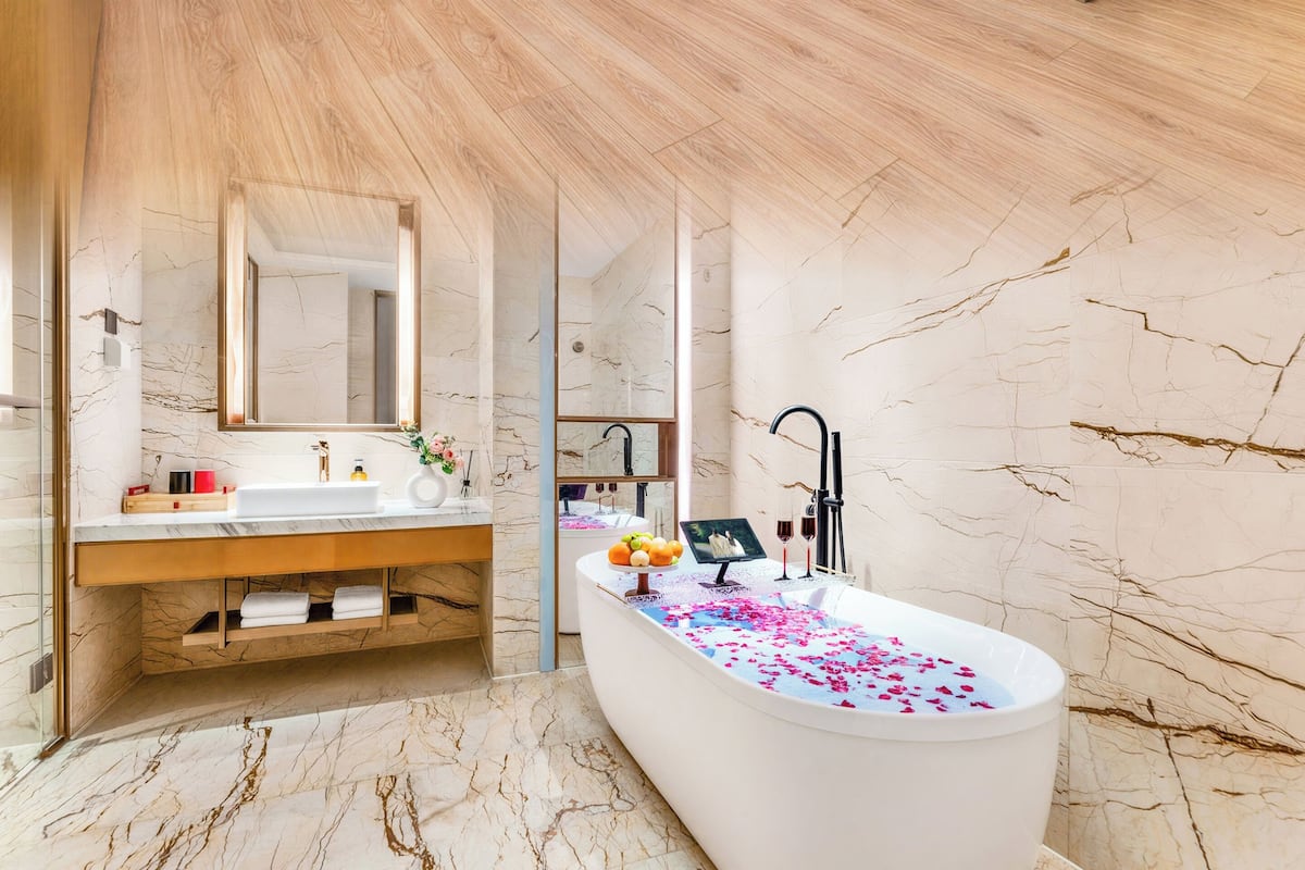 Ein modernes Hotelzimmer mit einem großen Bett, einer Sitzecke, einem Badezimmer mit Badewanne und einem Schminktisch mit Spiegel.