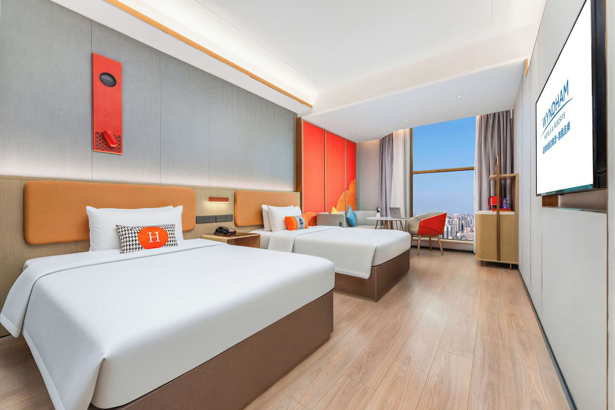 Ein modernes Hotelzimmer mit zwei Betten, einem Schreibtisch, einem Stuhl und einem großen Fenster.