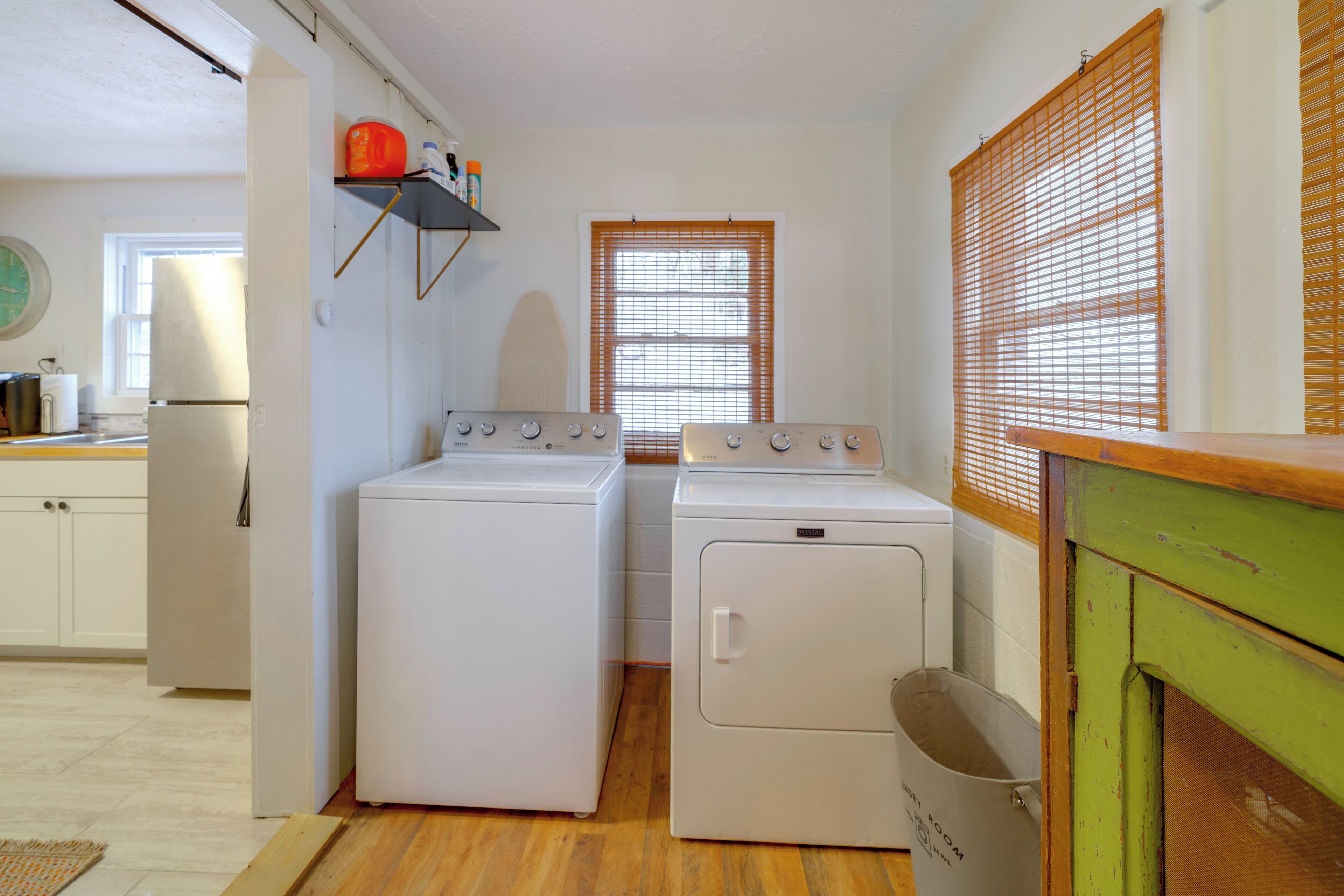 A compact laundry room with two washing machines and a dryer, wooden flooring, and a window with blinds.