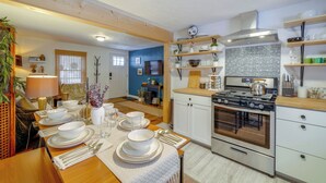 Una cocina moderna con armarios blancos, una estufa de acero inoxidable y un comedor con mesa dispuesta para cuatro.