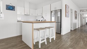 A modern kitchen with white cabinetry, a stainless steel refrigerator, and a wooden island with bar stools.
